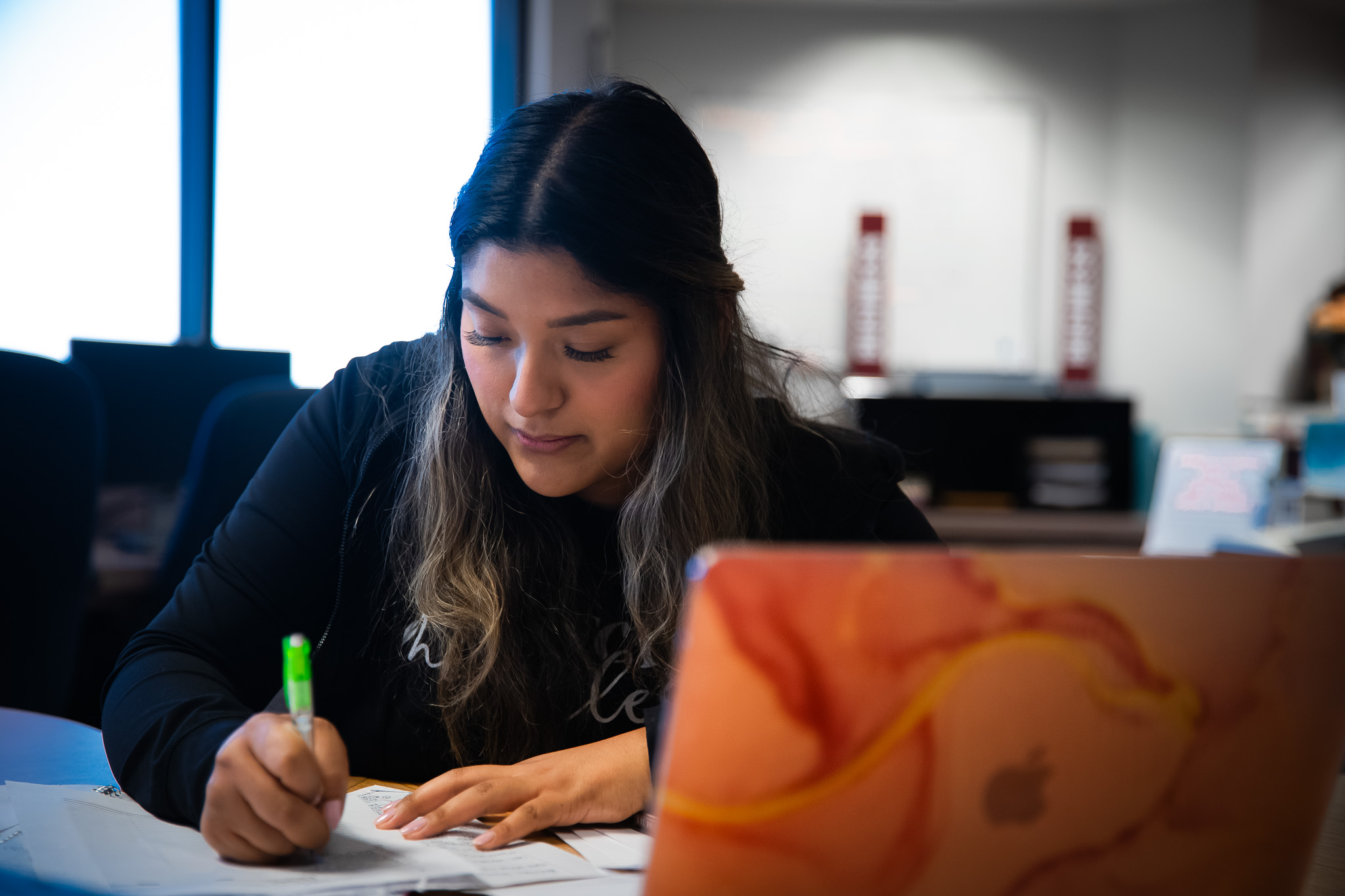 A student takes notes on paper while sitting in front of a laptop.
